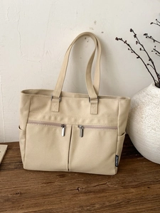 Minimalist beige canvas tote bag with dual front zipper pockets and brand label