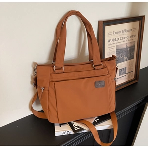 Detailed close-up of brown casual tote bag featuring a zipper pocket and a branded leather tag