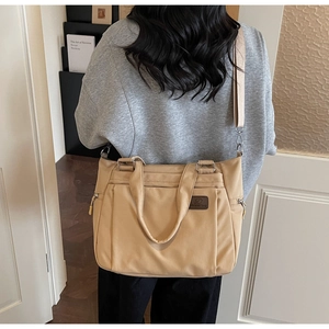 Detail of khaki nylon tote bag showing durable zipper pockets and leather logo patch