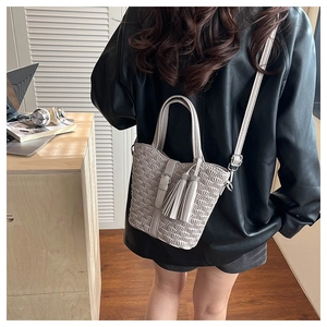 Detail of beige pleated bucket bag with tassel accent and adjustable shoulder strap