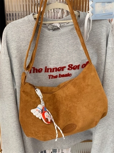 Detail of brown suede hobo bag featuring a cartoon pendant and logo on a grey sweatshirt