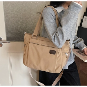 Detail of khaki nylon tote bag showing large front zipper pocket and adjustable strap