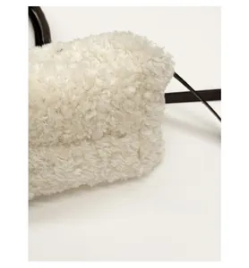Close-up of white faux shearling tote bag featuring reinforced bottom and black strap