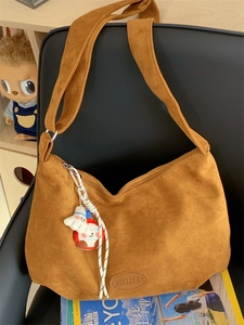 Detail of caramel suede tote bag with brand logo and cute charm on a leather chair