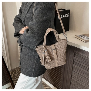 Detail of the woven texture and tassel pendant on the beige bucket bag for women