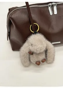 Nahaufnahme eines grauen Plüschhasen-Anhängers mit goldenem Verschluss an einer Ledertasche