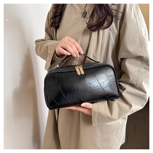 Detail of black crocodile-embossed handbag with dual golden zippers and handle