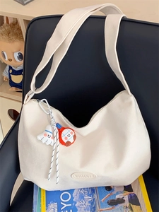 Detail of cream tote bag with leather logo patch and cute plush ghost charms on a chair