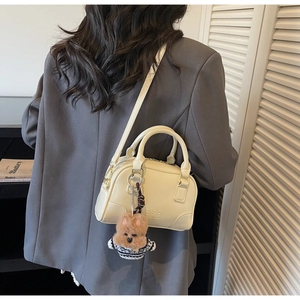 Detail of cream shell bag with brown plush bear charm worn with dark grey blazer