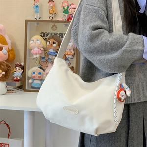 Close-up of white canvas shoulder bag with leather logo and cartoon doll keychain detail