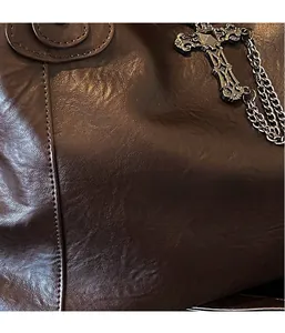 Detailed macro view of soft brown leather texture and gothic cross chain on the tote bag