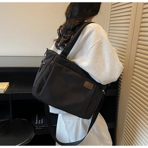 Detail of black nylon tote bag with leather logo patch and adjustable wide strap