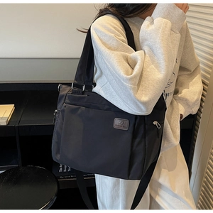 Detail of black nylon tote bag with leather logo patch and multiple storage pockets
