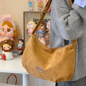 Detail of brown suede hobo bag featuring an oval logo patch and wide shoulder strap