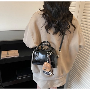 Detail of glossy black leather tote featuring dual metal zippers and cute dog plush pendant