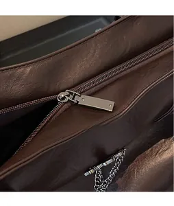 Detail of dark brown leather tote featuring smooth silver metal zipper and chain accent
