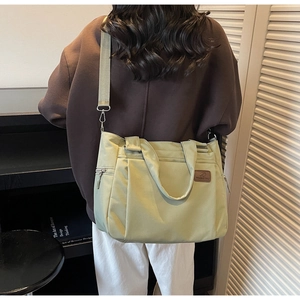 Detail view of light green tote bag showing brand logo patch and side zipper pocket
