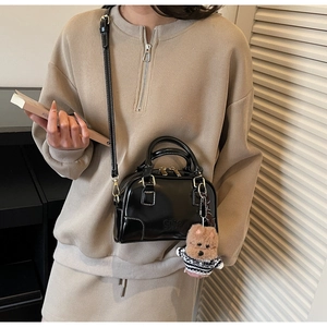 Detail of black glossy Boston bag with ciho logo and dog plush pendant on shoulder