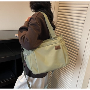 Detail of sage green nylon tote bag featuring adjustable strap and leather logo patch