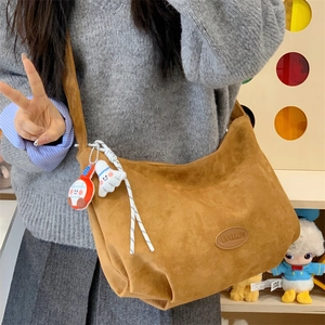 Detail view of brown suede hobo bag with cartoon plush pendants and logo patch