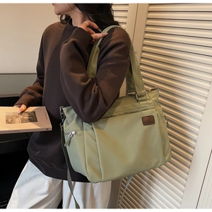 Detail of light green waterproof tote bag featuring multiple zippers and brown logo patch