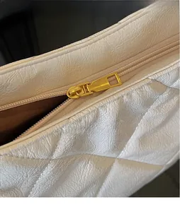 Close-up of golden zipper and quilted white leather texture on tote bag