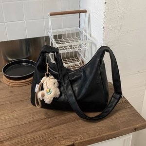 Close-up of soft black leather tote bag featuring a cute white alpaca plush keychain