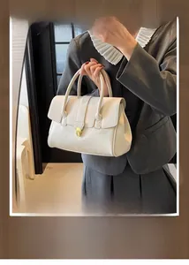Close-up of cream leather handbag with gold twist lock on a grey suit jacket