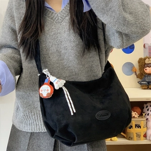 Close-up of black matte tote bag featuring oval leather logo patch and cute plush charms