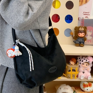 Close-up of black matte crescent tote bag featuring logo patch and cute doll charms