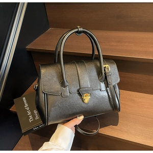 Detail of black leather briefcase bag with golden clasp and long strap on dark wooden steps