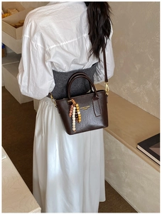 Détail du sac seau marron foncé avec pompon en perles et lettrage doré de mode