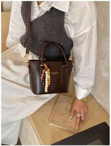 Détail d'un sac seau en cuir marron foncé avec lettrage doré et pendentif en perles