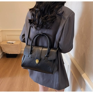 Model wearing black leather briefcase with gold buckle over a stylish grey suit jacket