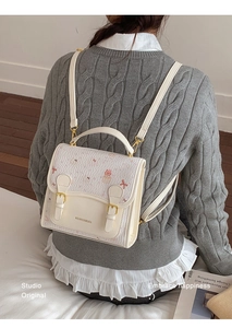 Detail view of a cream college-style backpack featuring cute bear embossing and gold buckle