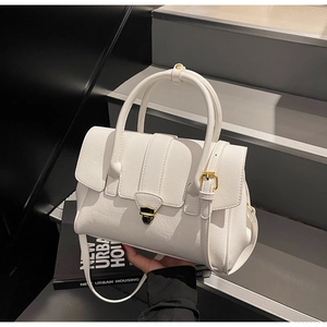 Detailed close-up of white leather handbag featuring a modern gold triangular metal clasp