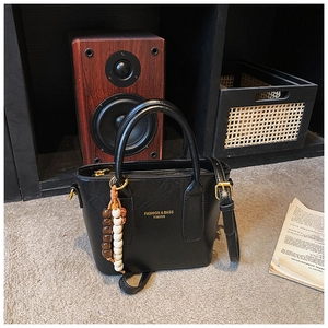 Détail d'un sac seau en cuir noir avec lettrage doré et accessoire en perles de bois