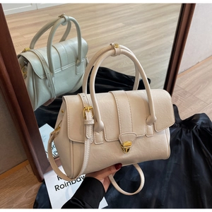 Detailed view of cream textured leather handbag with gold metal clasp and dual handles