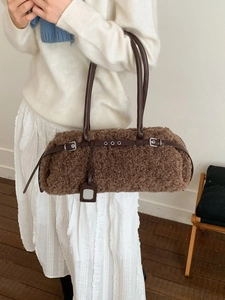 Brown faux shearling baguette bag with leather straps on a model in white outfit