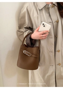 Détail du sac seau en cuir marron grainé porté par un mannequin en trench-coat beige