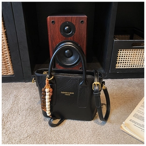 Détail d'un sac seau noir avec texture litchi et pendentif en perles sur bois sombre