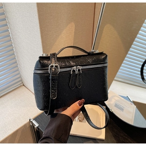 Close-up of black ostrich-embossed leather texture and silver double metal zippers on handbag
