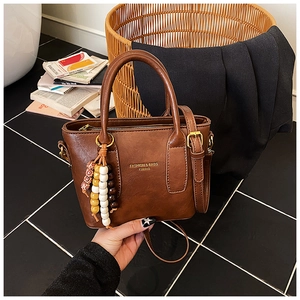 Détail du sac seau en similicuir marron avec breloque en bois et bandoulière longue