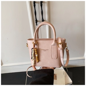 Détail du sac à main rose en cuir grainé avec texte doré et pompon décoratif en perles