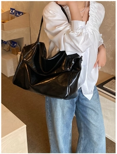 Close-up of black glossy hobo bag worn over the shoulder showing patent leather shine