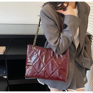 Quilted burgundy tote bag with chain strap shown on a model in a professional office setting