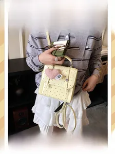 Detail of light yellow polka dot backpack with plush pink heart charm and metal snap