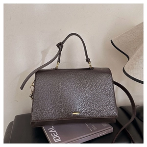 Détail d'un sac cabas en cuir marron foncé à grain litchi avec fermoir doré sur livres