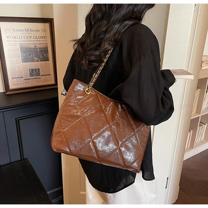 Detail of dark brown quilted tote bag with gold chain strap in a retro indoor setting