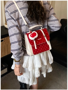 Detail of red polka dot backpack with plush heart charm and white leather straps